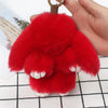 A bright red plush bunny keychain being held by a hand against a white background.