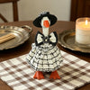 A handcrafted goose statue dressed in a black and white plaid dress with a bow and orange feet, displayed on a checkered mat.