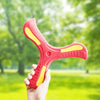 A hand holds a bright red soft foam boomerang flying disc with yellow accents in a green outdoor setting.