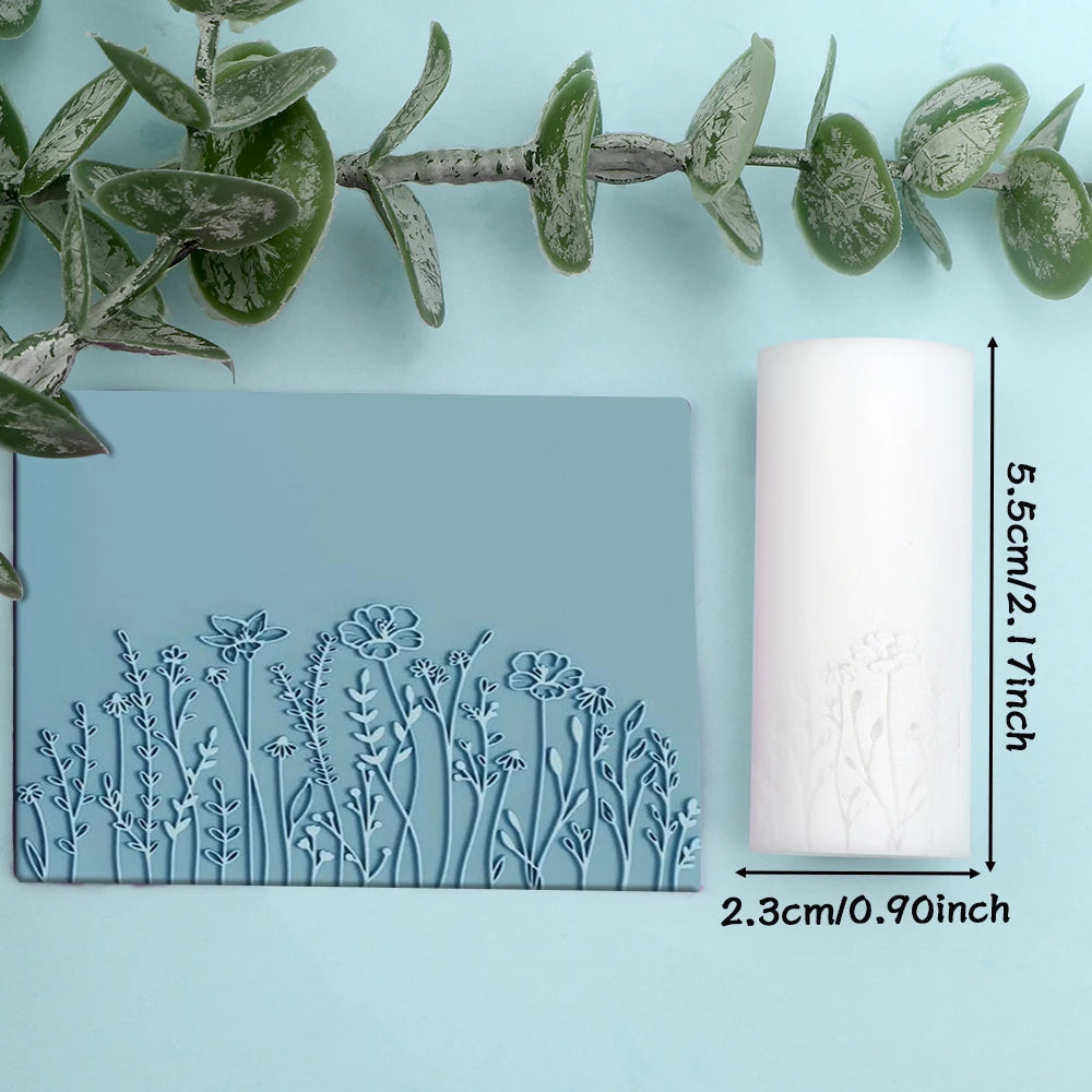 A light blue rectangular silicone roller with a detailed floral and leaf texture is shown next to a green plant branch.