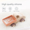 A beige silicone baby teether toy shaped like a cartoon car is shown nestled in white granular material.