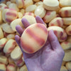 A hand holds a pink and white striped squishy toy, resembling a dog noodle, against a background of similar toys.