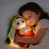 A young girl is gently holding a plush toy shaped like a green and yellow hooded figure with a crown, illuminated by a warm l