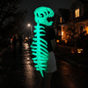 A person wearing a glow-in-the-dark dinosaur skeleton mask is walking down a dark, wet street at night.