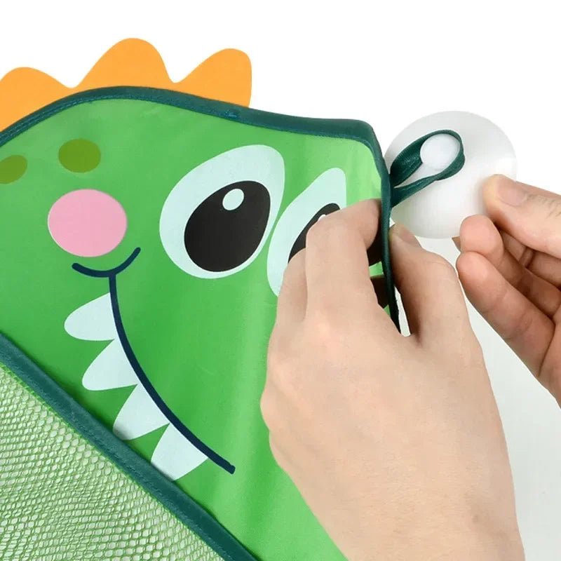 A hand is attaching a suction cup to a green and orange toy storage bag featuring a frog design.