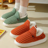 A pair of women's cozy faux fur slippers in olive green and bright orange, shown on a light surface.