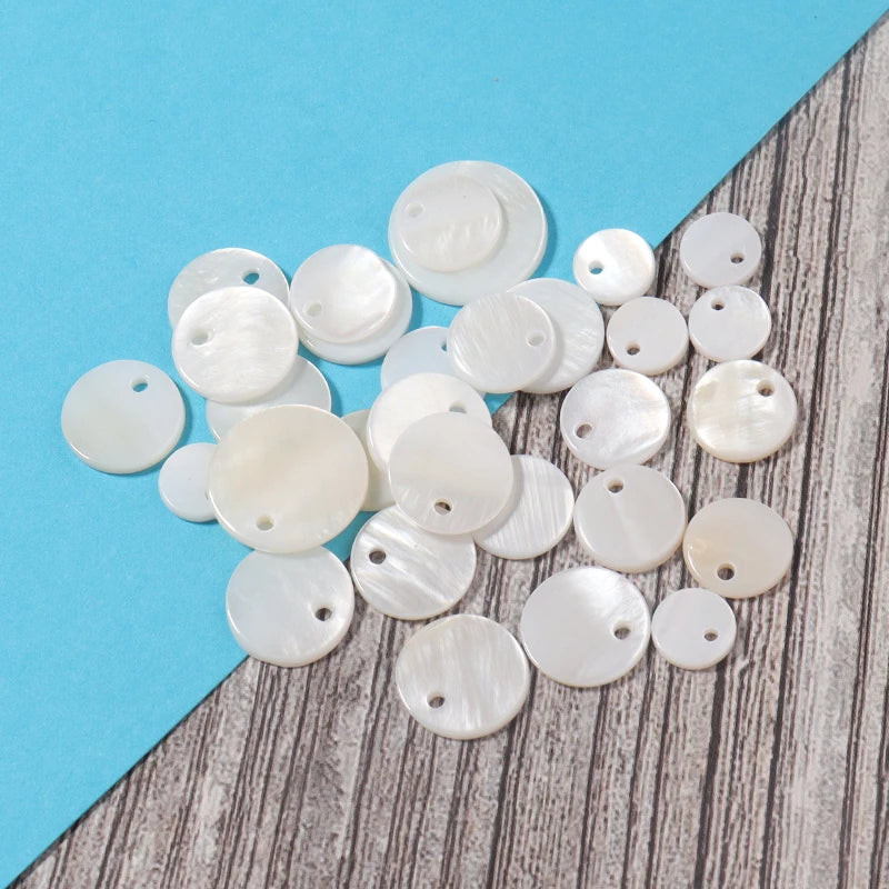 A collection of natural white shell beads in various round sizes and finishes scattered on a blue and gray surface.
