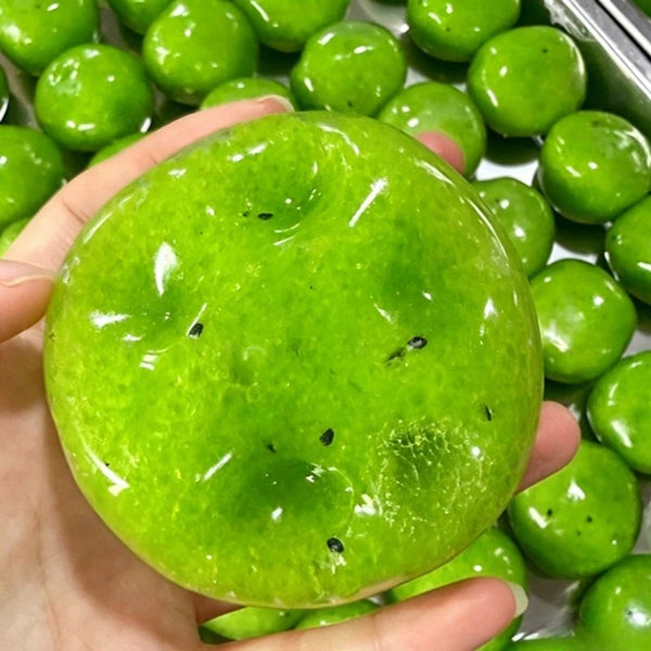 A bright green kiwi-shaped squishy fidget toy is held in a hand, surrounded by other similar toys.