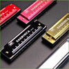 A collection of various harmonica models and cases, including a red, pink, and gold-colored harmonica with numbered holes.