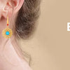 A close-up of a woman wearing a gold and blue teardrop earring.
