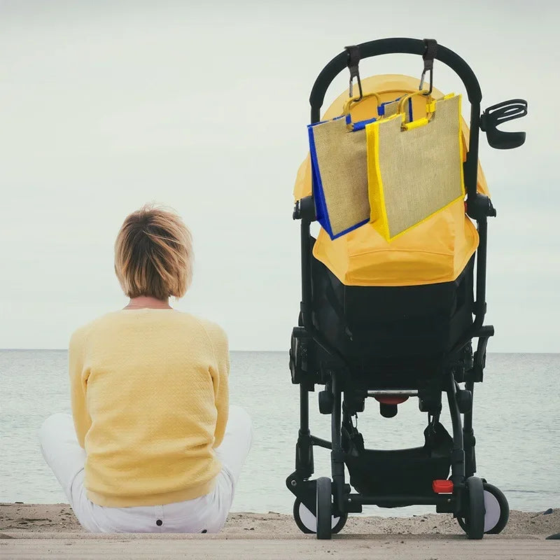 A person is sitting on the ground next to a yellow stroller with black hooks and nylon straps.
