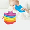 A young girl is holding and playing with a stack of colorful plastic cups and boats.