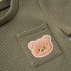 A close-up of a olive green knitted outfit featuring a cute, light brown bear print on the chest pocket.