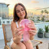 A woman holds a translucent pink jellyfish squish toy with dangling tentacles against a city skyline backdrop.