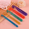 A set of three transparent crystal crochet hooks in purple, orange, and teal are displayed on a pink background.
