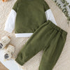 A moss green boys' two-piece sweatshirt set with white contrast panels lying on a cream textured rug.