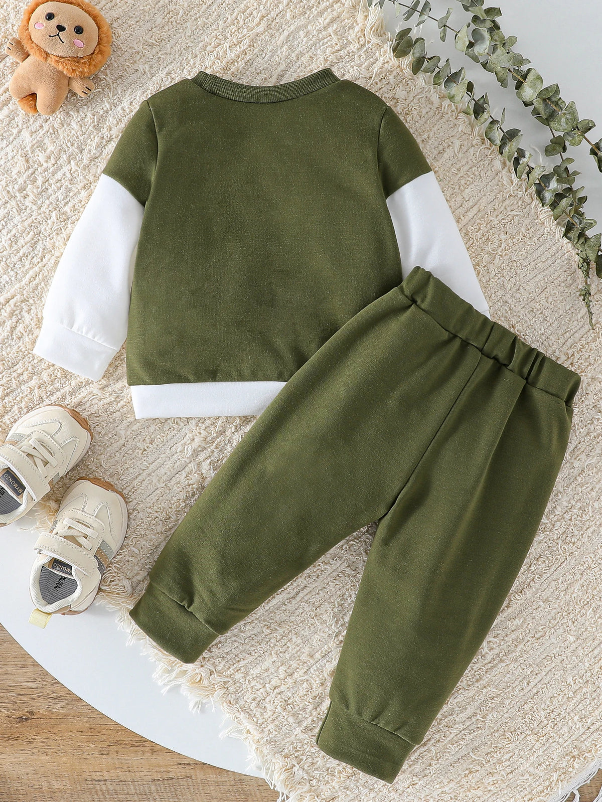 A moss green boys' two-piece sweatshirt set with white contrast panels lying on a cream textured rug.
