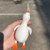 A hand holds an orange and white jumbo squishy duck stress ball fidget toy against a gray outdoor background.