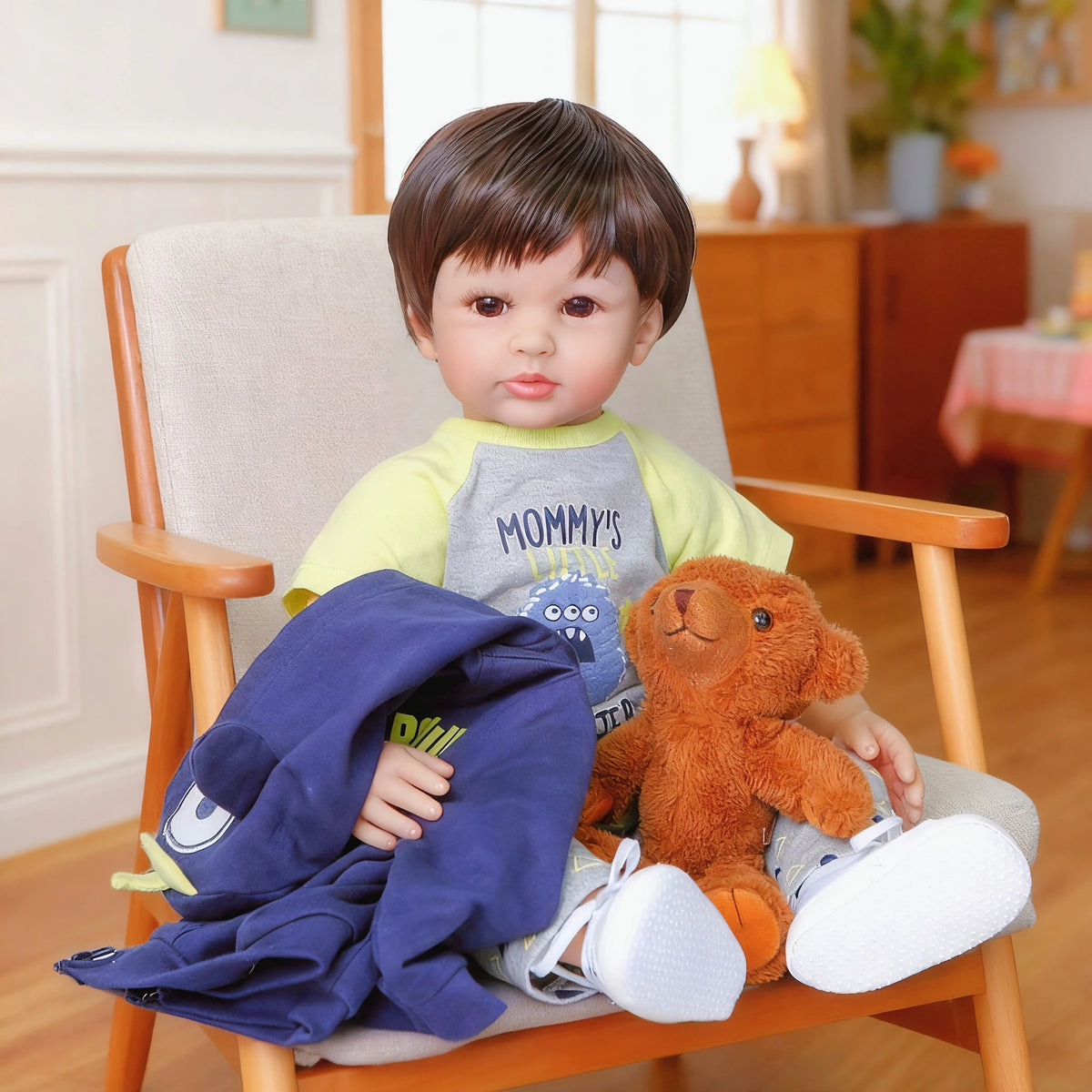 A baby doll with soft cloth body wearing a blue outfit sitting in a wooden chair.