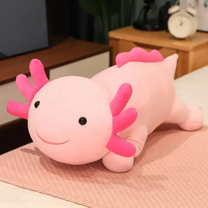 A pink axolotl plush pillow with pink gills resting on a light pink surface.