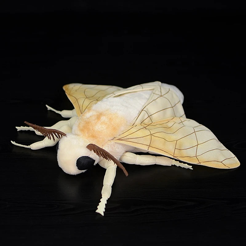 A soft, white and cream silk moth plushie with delicate wings and antennae against a dark background.