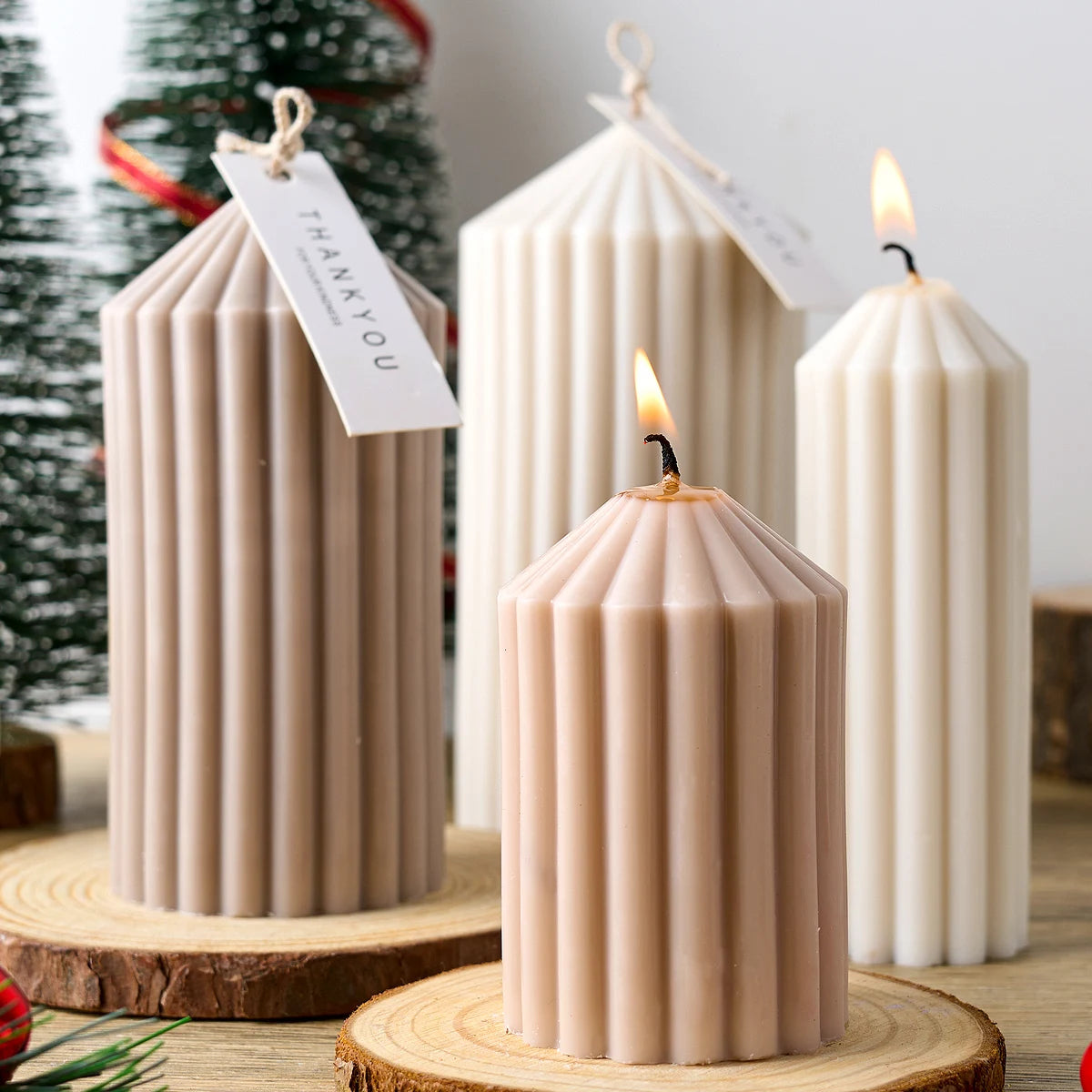 A tall, cylindrical pink silicone candle in a striped design sits on a wooden slice next to a lit candle.