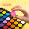 A hand is holding a portable watercolor paint set with various colored paint pots on a yellow surface.