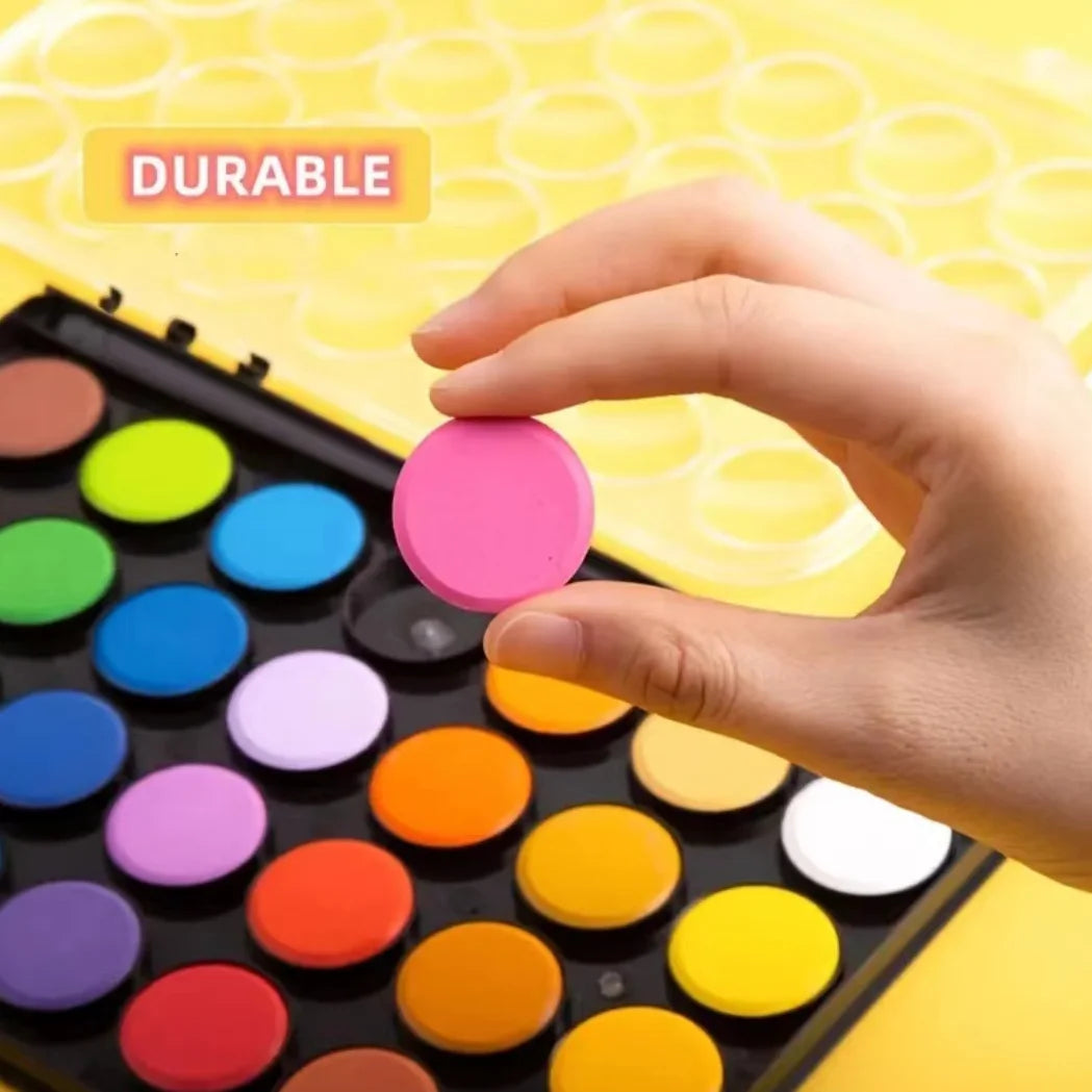 A hand is holding a portable watercolor paint set with various colored paint pots on a yellow surface.