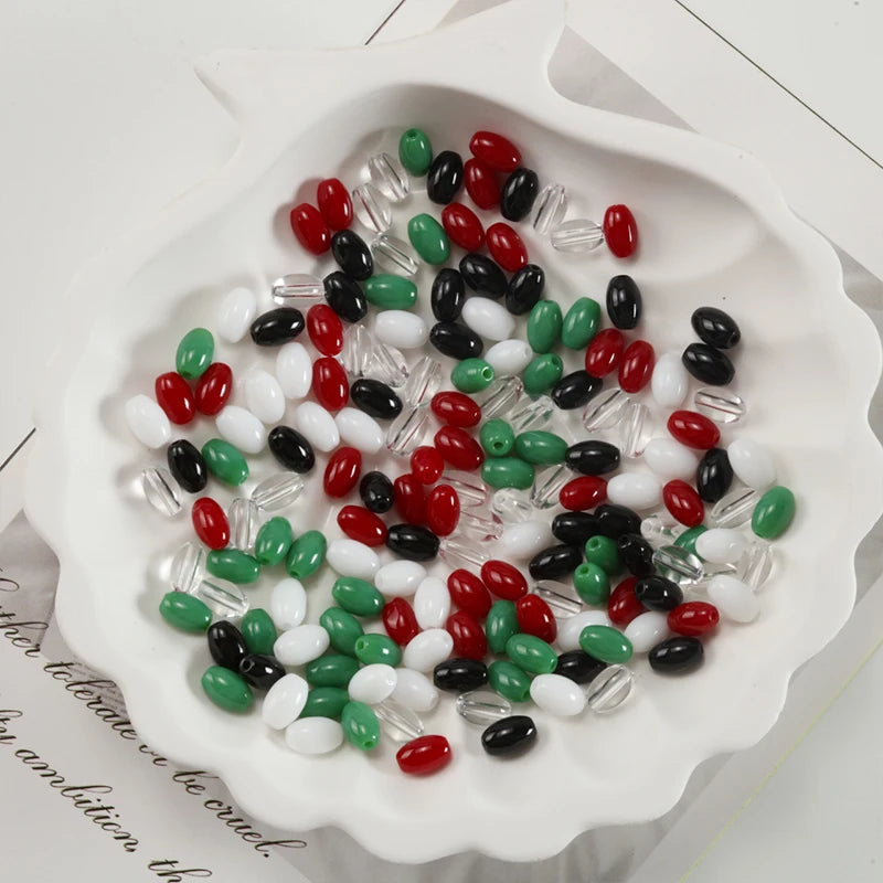 Oval glass rice grain beads in various colors including red green black white and clear are displayed in a white dish