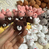A close-up of various handcrafted crochet animal keychains including rabbits, chicks, cats, and dogs in shades of pink, brown