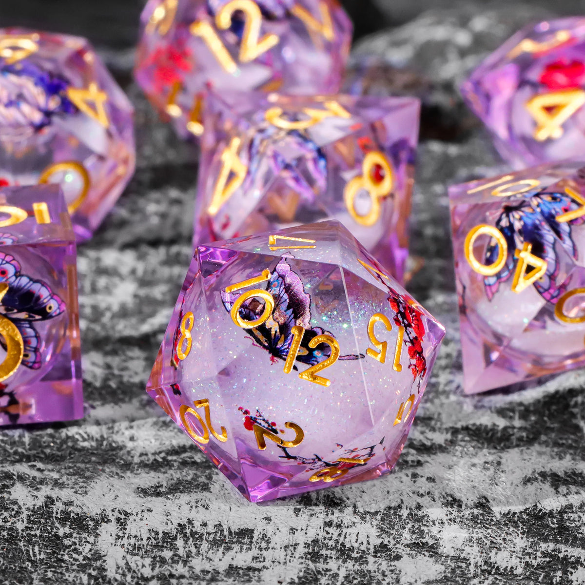 A collection of iridescent purple resin dice with gold markings and glitter, scattered on a dark surface.