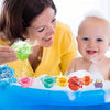 A woman is helping a baby play with colorful stacking cups bath toys in a blue basin.