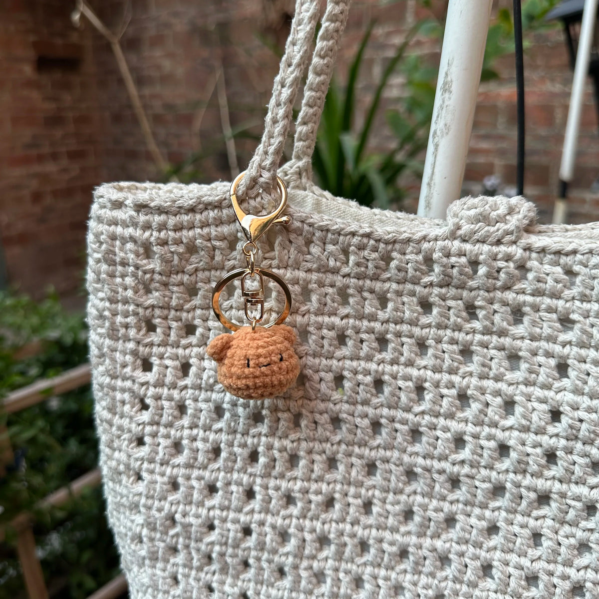 A handcrafted crochet animal keychain in a light beige color with a gold-toned metal loop.