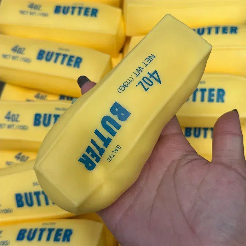 A hand holds a yellow butter stick squishy stress ball with the text 402 BUTTER SALTED visible on the packaging.