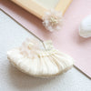 A delicate cream mini doll wedding dress outfit set with floral accents resting on a pink surface.