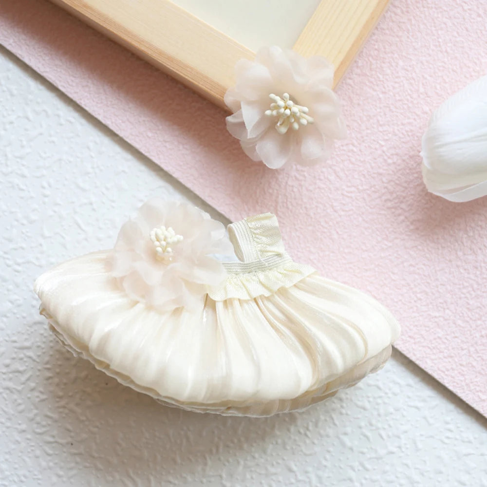 A delicate cream mini doll wedding dress outfit set with floral accents resting on a pink surface.