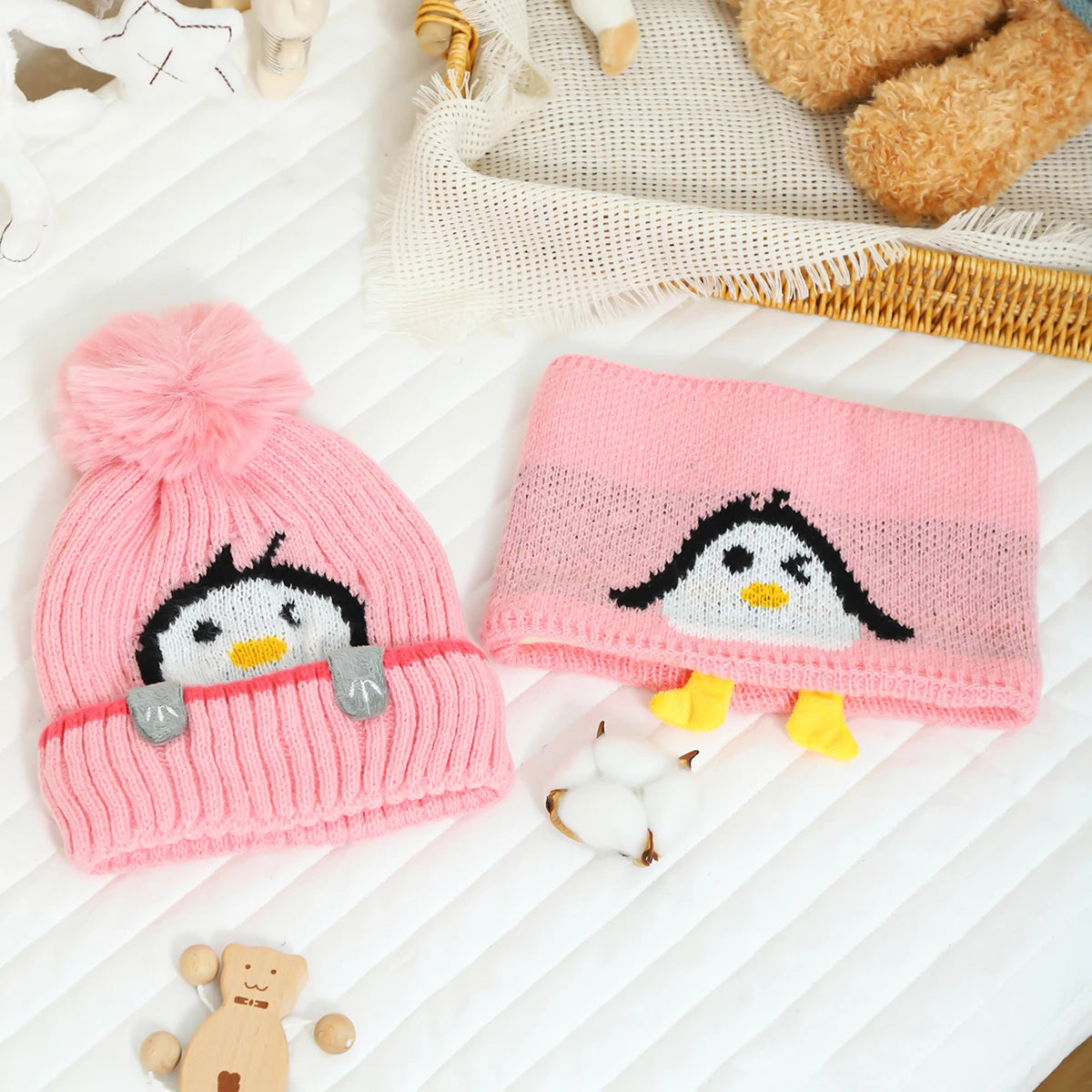 A pink knit penguin hat and scarf set with yellow accents resting on a white surface.
