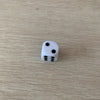 A single white die with five pips is shown on a light wooden surface.