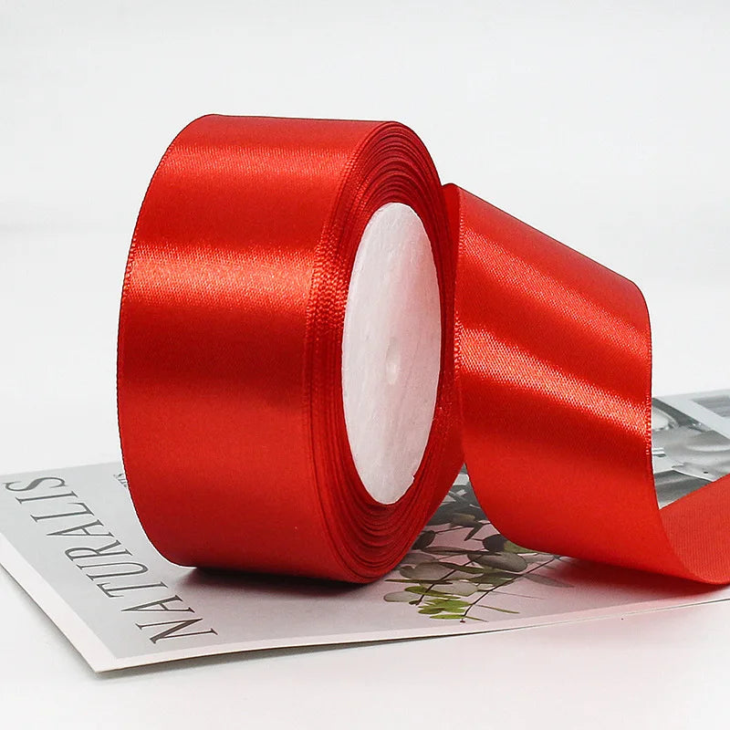 A roll of red satin ribbon used for gift wrapping or crafts, shown next to a sheet of paper.
