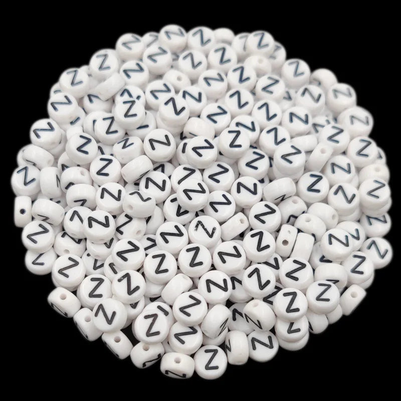 A pile of small white acrylic alphabet letter beads, including the letter N, for jewelry making.