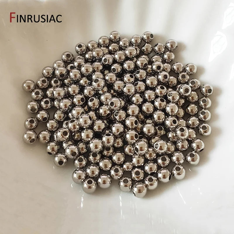 A pile of small, round, silver-colored spacer beads for jewelry making on a white surface.