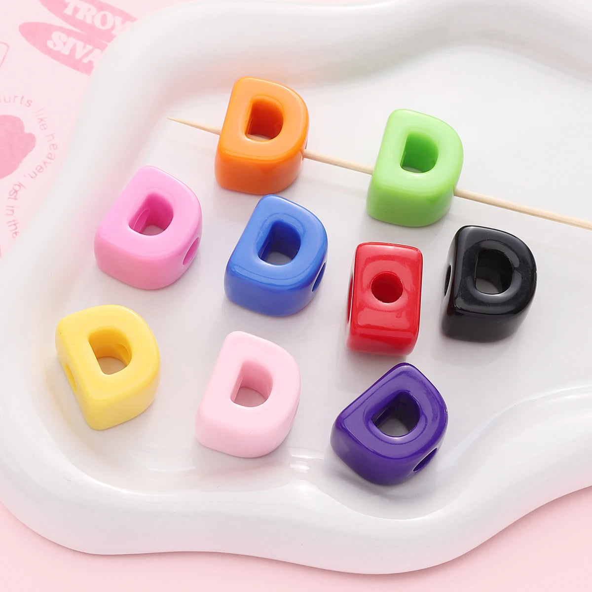 A collection of colorful acrylic letter beads in various shades including orange, green, pink, blue, yellow, and purple arran