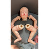 A realistic reborn baby doll kit with painted details and a cloth body is positioned on a dark surface.