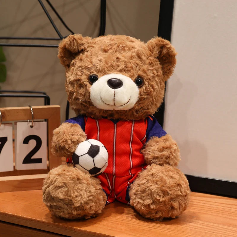 A fluffy brown bear plush toy wearing a red and blue football jersey sitting on a wooden surface.