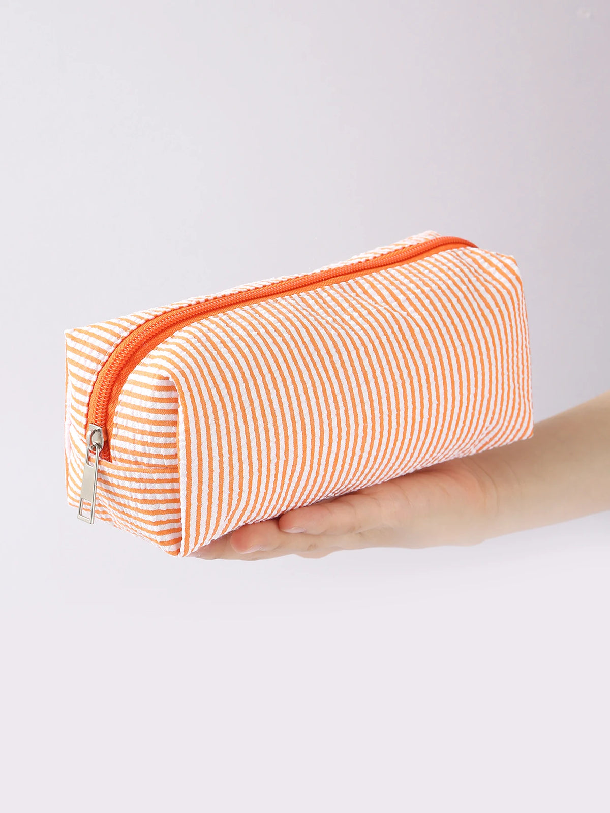 An orange and white striped canvas pencil case with a zipper is held in a hand.