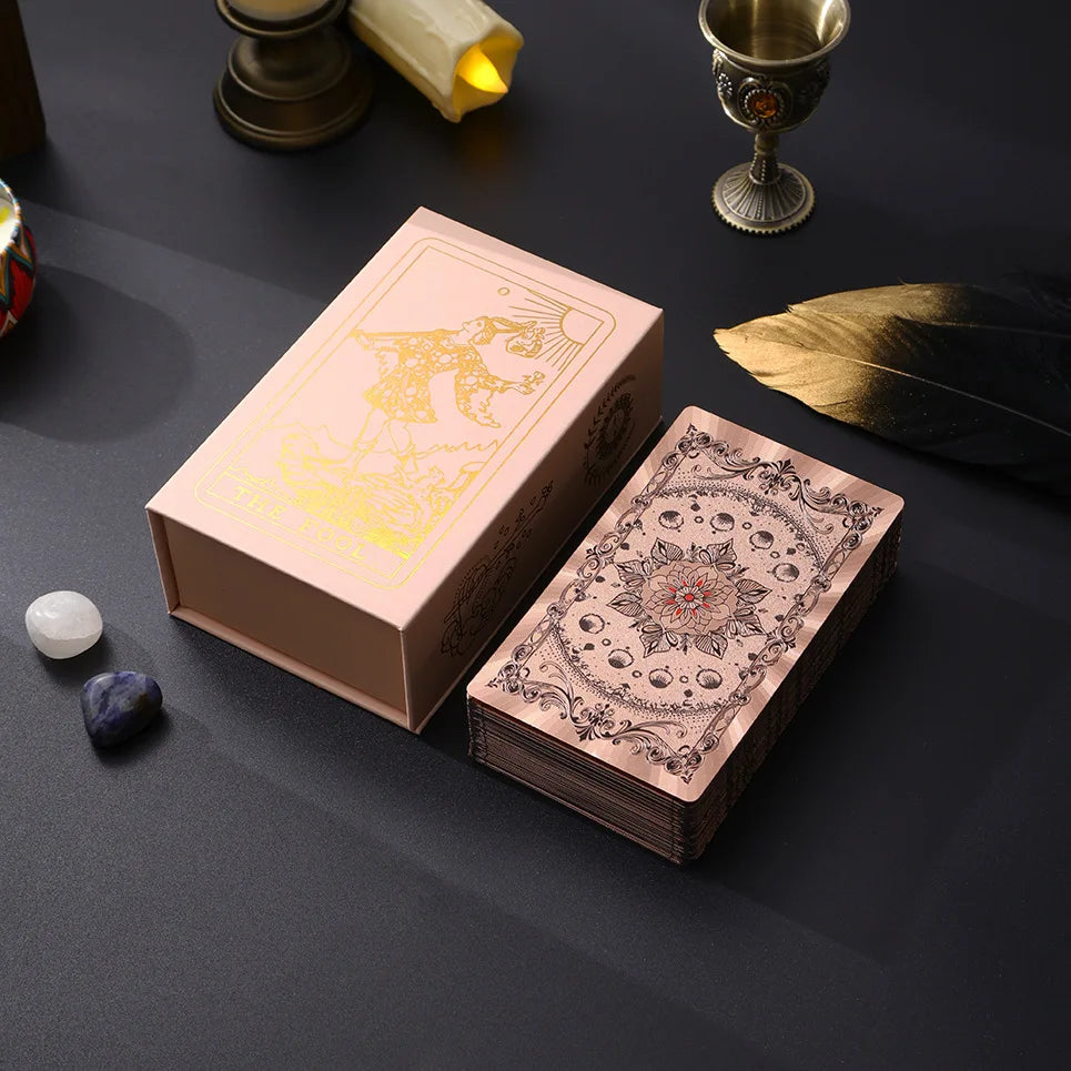 A box of gold foil tarot cards with a rose pink oracle finish resting on a dark surface.