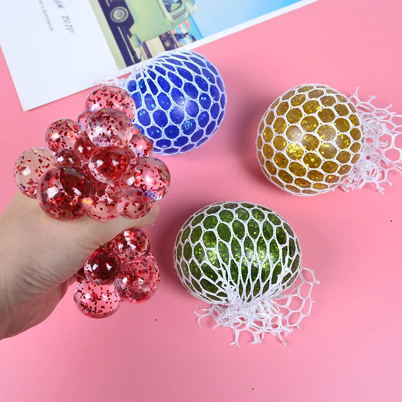 A hand holds several colorful squeeze stress relief balls, including blue and red ones with mesh netting.