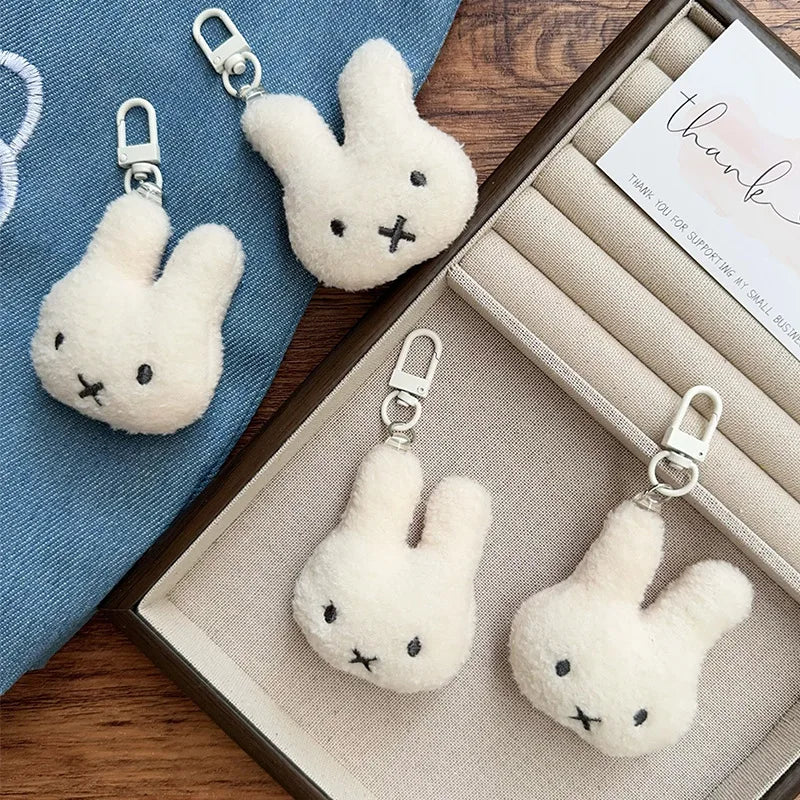 Two white Miffy cartoon rabbit keychains displayed in a wooden box with a blue cloth background.