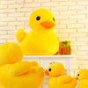 A close-up of a bright yellow plush toy duck sitting on a white shelf against a brick background.