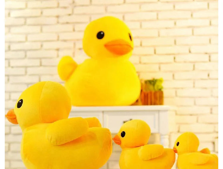 A close-up of a bright yellow plush toy duck sitting on a white shelf against a brick background.
